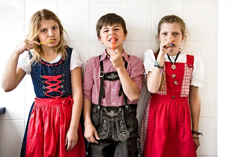 Drei Kinder in Dirndl und Lederhose beim gemeinsamen Zähneputzen.
