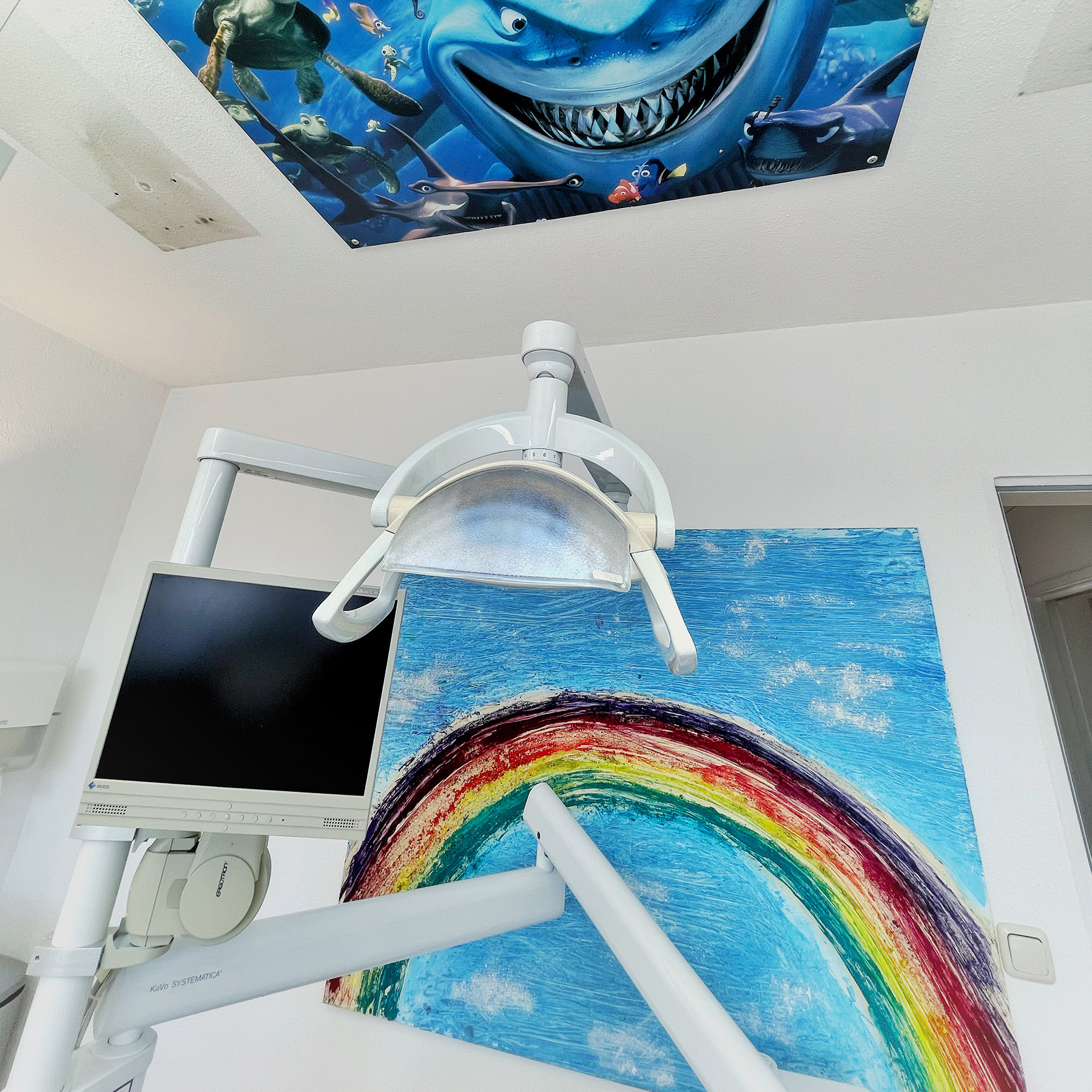 Behandlungszimmer mit farbenfrohem Regenbogenmotiv und Haifischillustration an der Decke.