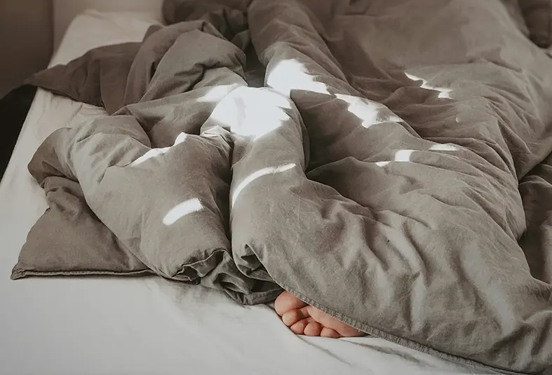 Person unter einer Bettdecke mit sichtbar herausragendem Fuß.
